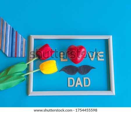 Creative  Happy  Father  Day  Concept  setting  with  necktie,artificial  tulips,blank  wooden  picture frame,red  heart  shape  and  the  text  on  blue  background