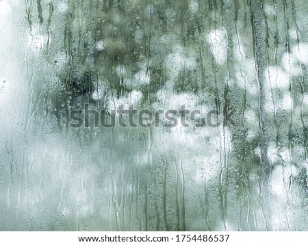 Fogged window glass with rain drops. Background with copy space for text. Rainy art texture. Green colors on blurred background.