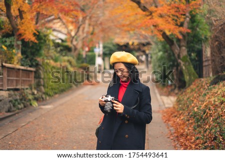 Young happy Asian woman looking to camera for checking picture and walking in beautiful autumn park, Tokyo, Japan, Asia. Lifestyle and travel concept
