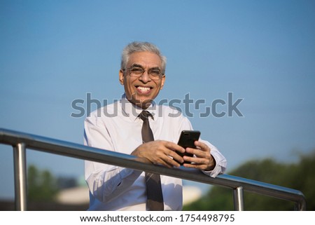 
Senior businessman standing near iron fence and texting