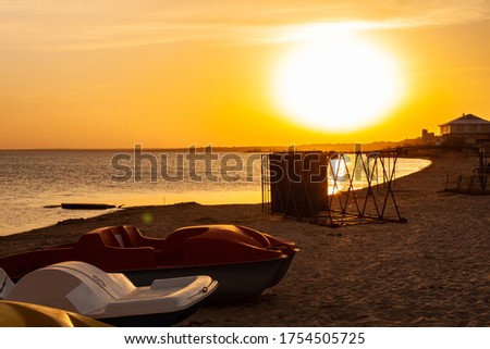 Pedal boats on the sunset on a tropical island beach. Colorful catamaran on an empty sea shore on evening landscape with sun rays. Wallpaper for desktop, poster, marine travel photo, post card design.