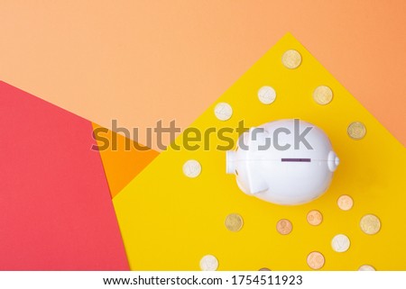 White piggy bank with euro coins around viewed from above with a warm colored background made from card stock