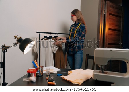 The seamstress stands beside the hanger with clothes making a choice. The concept of trying on a sewn sewn adecey in a studio.
