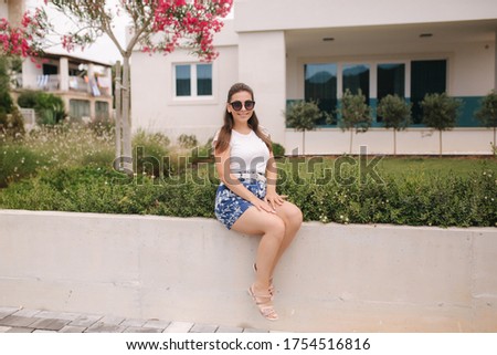 Attractive woman sits by the house in summer time. Beautiful young woman have a rest in front of her house