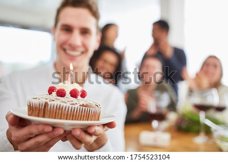Young man gives cake with candle for birthday to friends in the kitchen