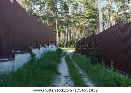 an alley with two brown metal fences and a passage with an expensive overgrown green grass