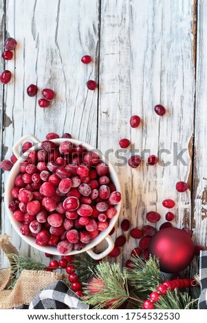 Frozen cranberries in a bowl over a white wood table background with Christmas decorations. Top view.