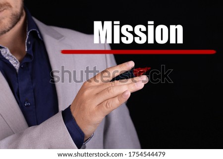 Businessman hand writing MISSION with red marker on a black background, business concept.