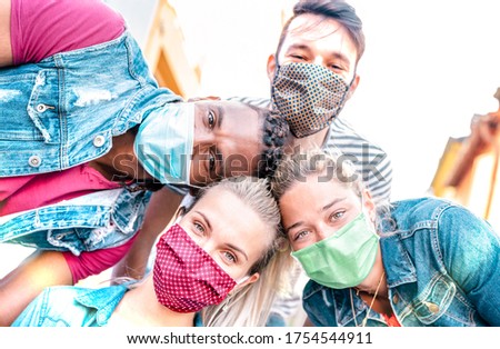 Multiracial millenial friends taking selfie smiling behind face masks - Happy friendship and new normal concept with young people having fun together - Bright sunshine filter with focus on left girl Royalty-Free Stock Photo #1754544911