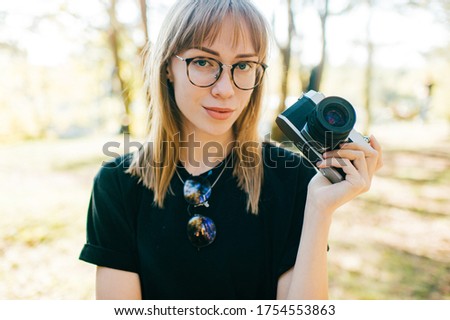 Portrait of beautiful young female photographer with short fair hair in black t-shirt take photos of nature in the summer forest.