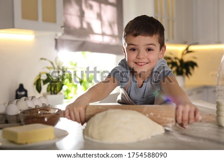 Cute little boy rolling dough at table in kitchen. Cooking pastry