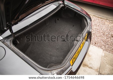 Inside the boot compartment of a mx5 with black carpet completely clean and empty trunk compartment open. Parked on gravel and paving 