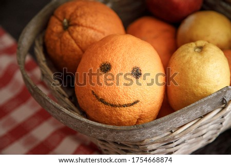 basket of oranges, one of which drawn a smile inside a wicker basket on a table with checkered tablecloth