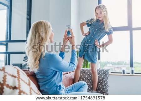Caucasian woman making photo on mobile phone of her daughter while having fun at home