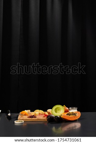 still life with glass yogurt and fruit on top of a grey table and black curtains background