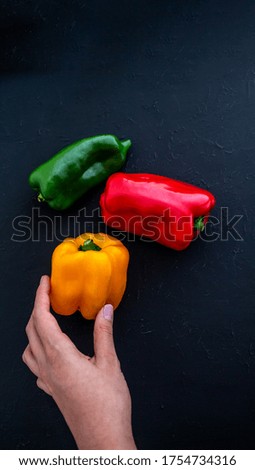A female hand is holding a yellow pepper that is next to another one of different colors on a rustic surface