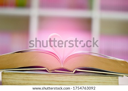 Open book with page of the book rolled into a heart colorful blurred background. Focus on book and shallow depth of field. Education, Valentines day concept.