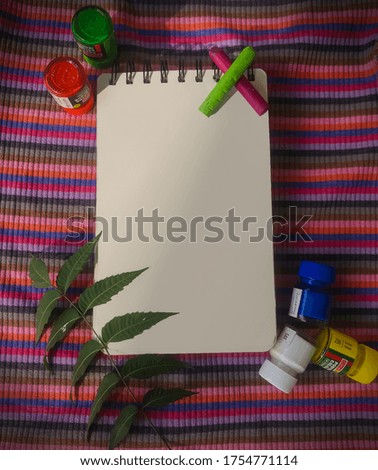 Blank Notebook/ art book with and colors and leaves on colorful background.Table top photo of workspace.