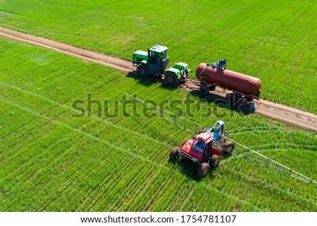 Tractor field treatment with herbicides. The farmer pours a chemical into the sprayer. Next to it is another tractor with a water tank. Shooting from a drone.