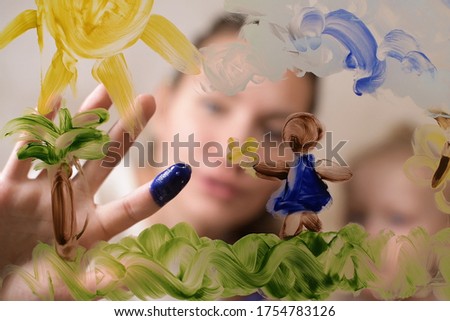 Mom teaches a child to draw by sliding her daughter s fingers on glass and dipping in paint. Selective focus