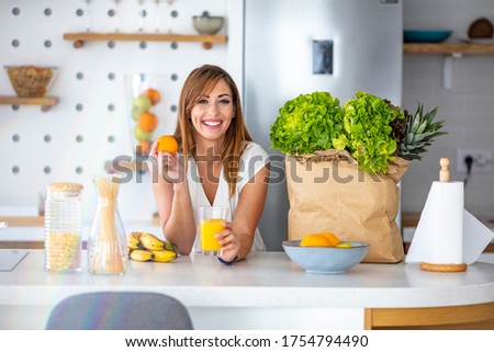 Enjoying a well-balanced breakfast. Smiling woman drinking orange juice. Beautiful young woman with glass of orange juice at kitchen table. Young beautiful woman in kitchen drinking juice