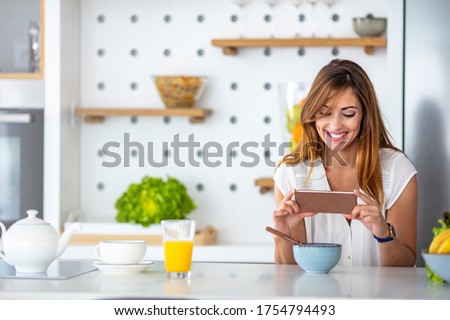 Woman in the kitchen taking photo of prepared breakfast. Beautiful woman in kitchen using mobile phone. Ready to make her own recipe book. Woman taking a picture of breakfast on her kitchen table