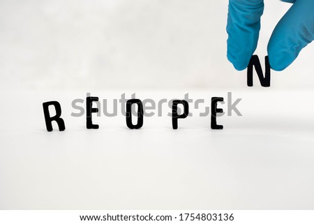 The word reopen in black letters against a plain white background.  Letter N added by a hand in a blue medical protective glove.  Concept image of business reopening post corona virus lockdown