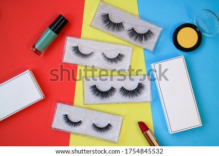 Top view of false eyelash extension with colorful background and make up fashioned accessories such as eyes shadow, lipstick and nail polish 