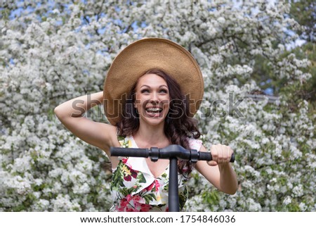 Cheerful, young woman rides a scooter.
Background blooming apple trees.
Concept: hello spring, summer.
Quarantine exit
