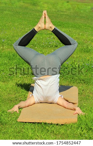 Young woman of European appearance does yoga in summer nature. Woman standing in pose closed angle headstand, badhakona shirshasana. High quality photo for web and print with empty space for text and