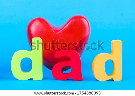 Happy Father's day. Red heart and the inscription "Dad" from multicolored wooden letters  on blue background. Selective focus.