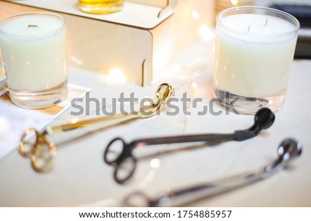 Wick golden, black, silver metal scissors for extinguishing white aroma candles in glass cups are lying on the table. Modern fashionable and comfortable accessory for home. Royalty-Free Stock Photo #1754885957