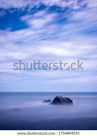 A tranquil tall seascape with rocks and flowing misty water and clouds