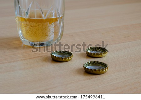 Semi-empty glass glass with beer and beer caps. Unfinished light beer and three corks on the table. Eye level shooting. Selective focus.