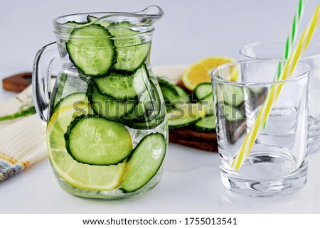 Cold drink made of cucumber and lemons, homemade lemonade in a decanter and two empty glasses, on a white background, shallow depth of field, selective focus. Healthy drinks concept