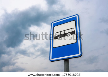 A low angle shot of a bus stop sign with a background of blue cloudy sky