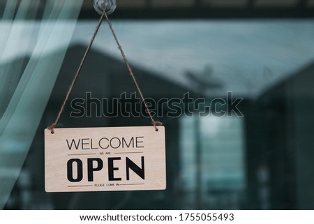 Label 'Welcome We are OPEN Welcome in' notice sign wood board hanging on door front coffee shop.