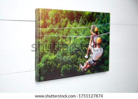 Canvas print. Stretched photo hanging on a white wooden wall, front view. Color photography with image of people on zip line. Interior decor