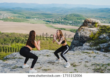 Two girls play sports keeping their distance. Playing sports in the mountains. Sports in quarantine. Sports exercise half-sit.