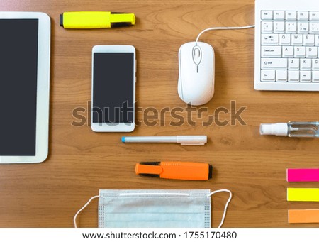 Gadgets, white computer keyboard and Stationery Supplies close with a hand sanitayzer and protective medical mask on a wooden background. Home office concept.