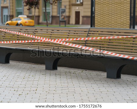 Tape fence across the bench. No people. Desert street in the spring day. Concepts - Stay at home, save live, self-isolation. Coronavirus Pandemic lifestyles