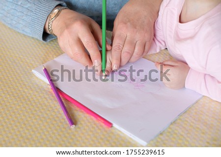 Grandmother teaches little granddaughter to draw. She takes a child s hand and draws out patterns with a pencil, close-up without faces