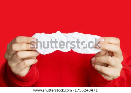 Women's hands hold a piece of white crumpled paper on a red background. Close-up, space for text and layout, space for copying,