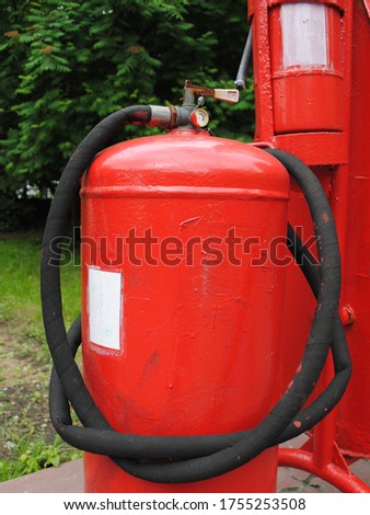 A large red fire extinguisher is at the gas station for quick elimination of fire. A gas station is a place where security measures must be at the highest level