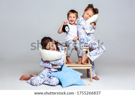 Three children in pajamas on a white background. Two girls are sleeping, the younger brother is cunningly looking and holding an alarm clock Royalty-Free Stock Photo #1755266837