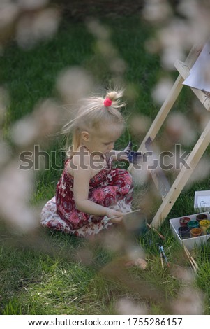Little girl in nature paints on an easel under a blooming cherry