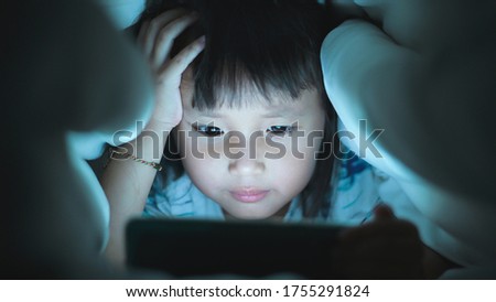Eye close up Little Girl are watching video in tablet on bed at night time light flashes reflected from the screen,children using games with addiction and cartoon concepts
