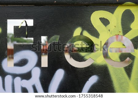 Free word on a graffitied metal panel with engraved see through letters with an unfocused industrial background.