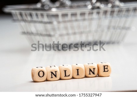 Online-an inscription made of wooden cubes on a white background and a metal shopping basket. Online sale.