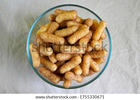 glass bowl with gluten-free corn sticks with cocoa on a beige tablecloth top view . sweet Breakfast snacks for children